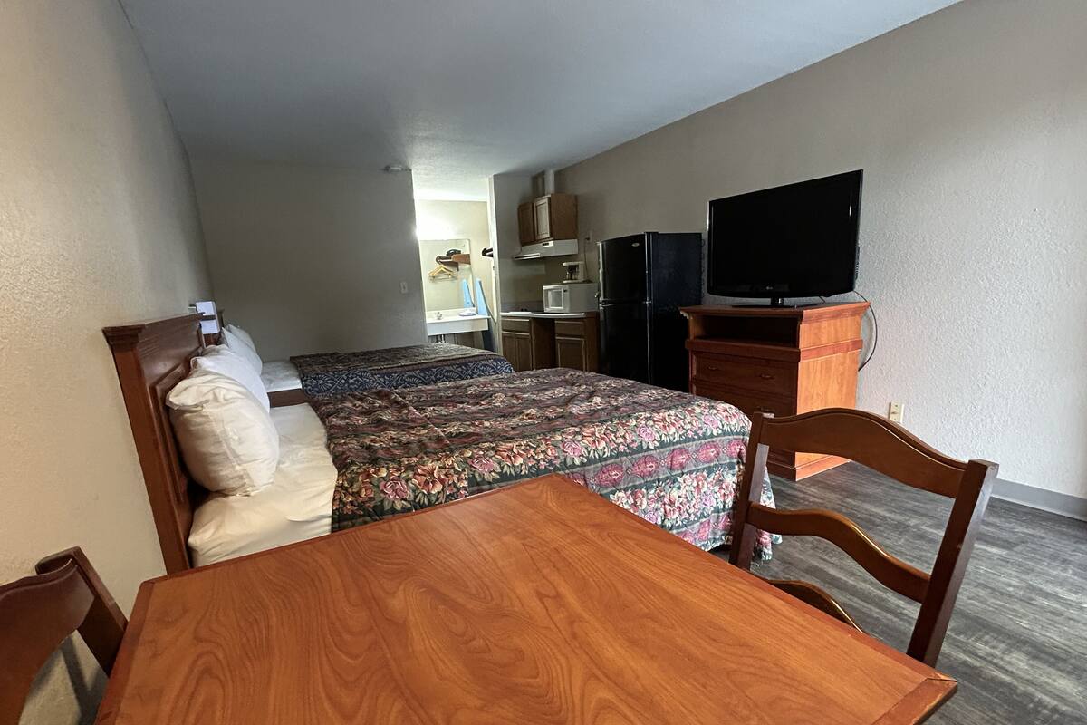 A bedroom with a bed, a wooden table, a TV, and a dresser.