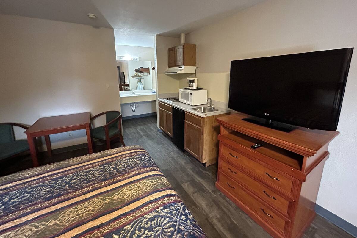 A compact hotel room with a bed, a television, a small kitchenette, and a desk.