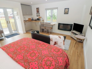 A bedroom with a bed, a TV, a kitchen area, and a dining table.