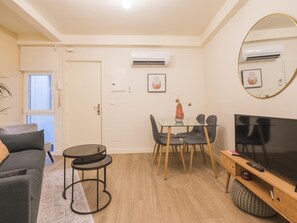 A modern living room with a sofa, a glass dining table with chairs, a TV on a wooden stand, and an air conditioning unit on the wall. - Comercio 37 (Toledo)