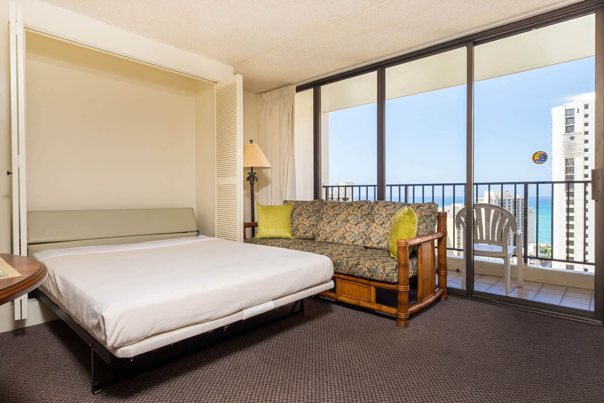 Habitación de hotel con cama, sofá, sillón y balcón con vistas a la ciudad.
