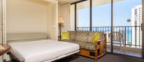 Habitación de hotel con cama, sofá, sillón y balcón con vistas a la ciudad.
