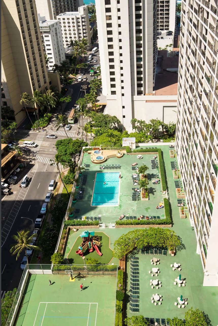An aerial view of a hotel with a rooftop pool, tennis courts, and a children's play area.