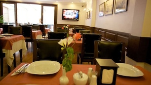 Un restaurant avec des tables dressées, un téléviseur fixé au mur et des tableaux encadrés qui ornent les murs.