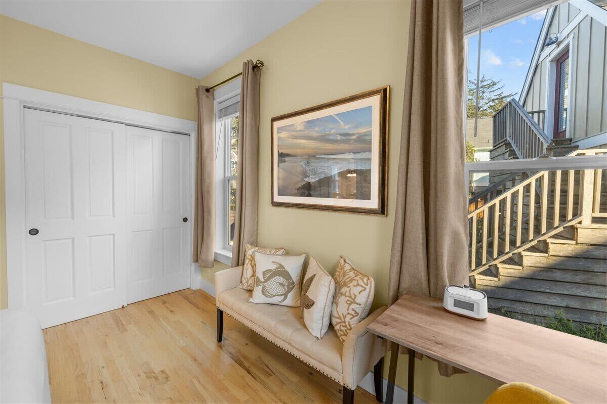 Una habitación con sofá beige, un cuadro en la pared, una ventana con cortinas y vista a una escalera de madera en el exterior.