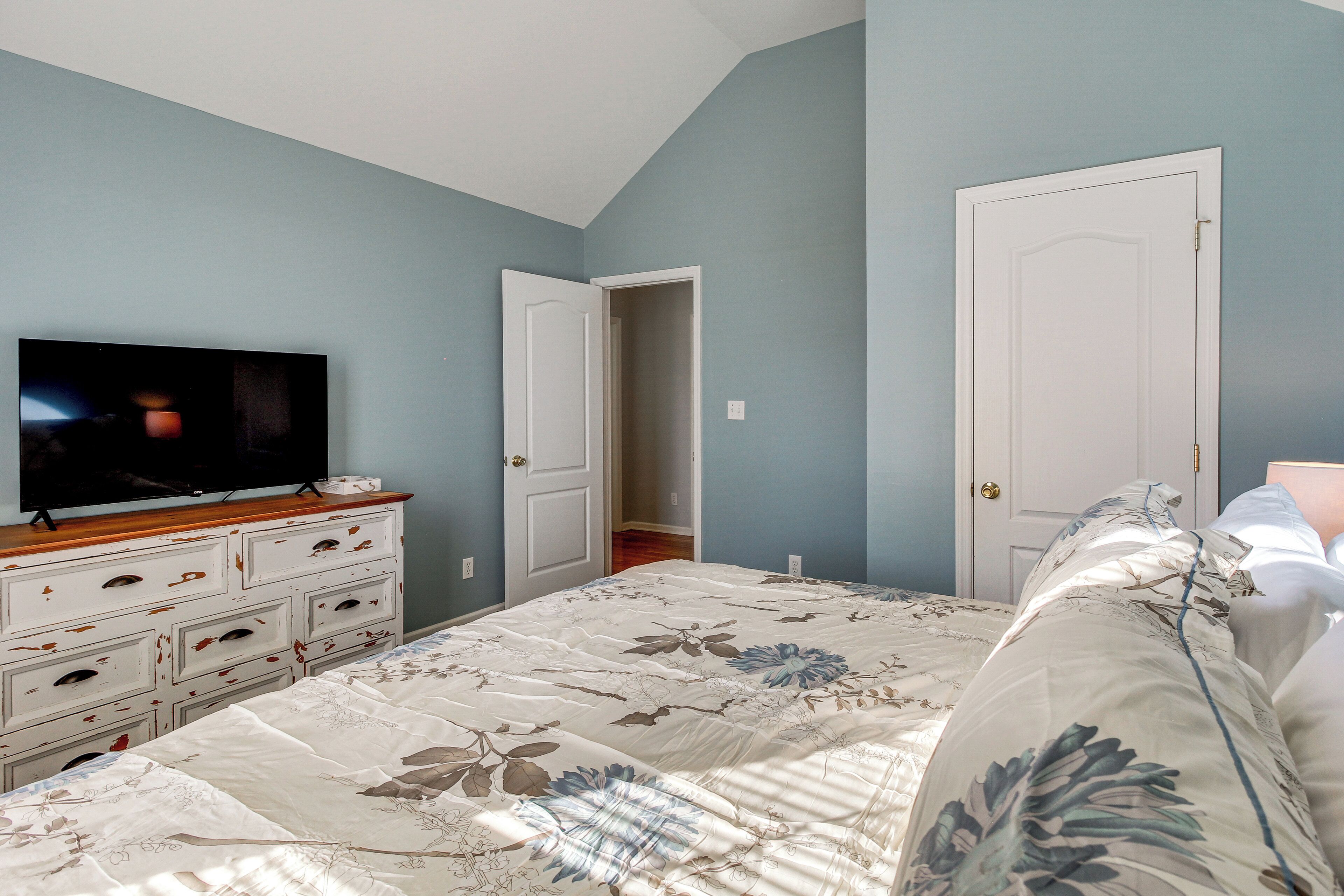 A bedroom with a bed, a dresser, a television, and two doors.