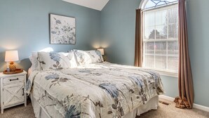 Une chambre à coucher avec un lit, une table de chevet, une lampe et une fenêtre avec des rideaux.