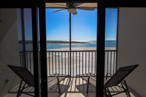 Un balcón con dos sillas, un ventilador de techo y vista a la playa.