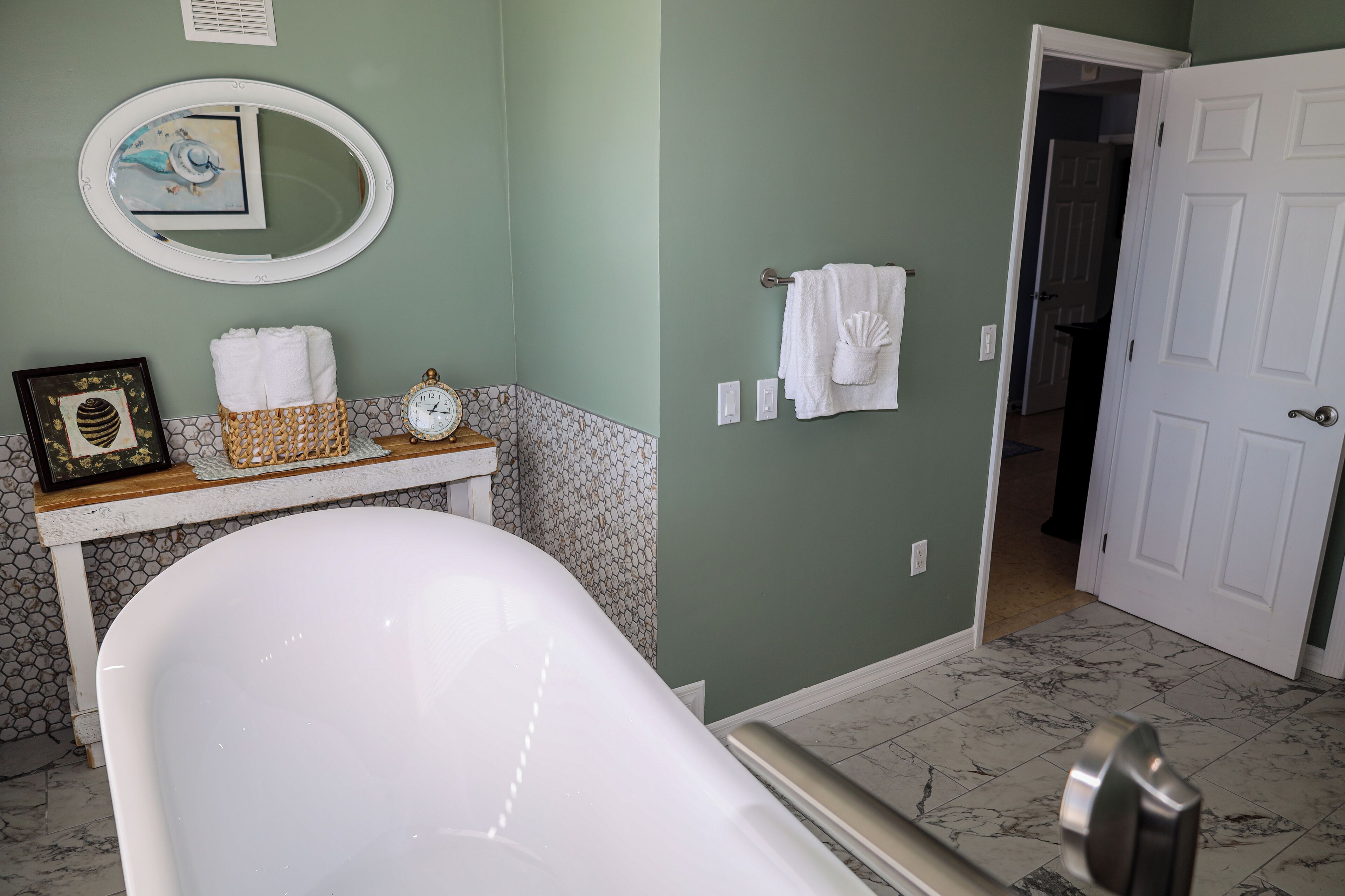 A bathroom with a freestanding bathtub, a vanity with a mirror, and a door leading to another room.