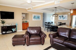 A living room with a brown leather sofa, a television, and artwork on the walls. - Luxury Fort Myers Beachfront Penthouse - Sunset Views & Pool (Fort Myers Beach)