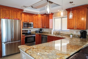 A kitchen with wooden cabinets, stainless steel appliances, granite countertops, and pendant lighting. - Luxury Fort Myers Beachfront Penthouse - Sunset Views & Pool (Fort Myers Beach)