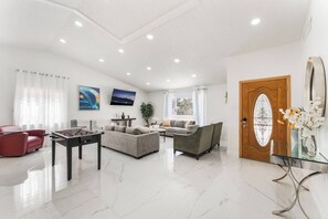 A spacious living area with a foosball table, sofas, a TV, and a door with a decorative glass panel. - NEW 5BR 4.5BA Home, Pool, BBQ, 8 min to Strip (Las Vegas)