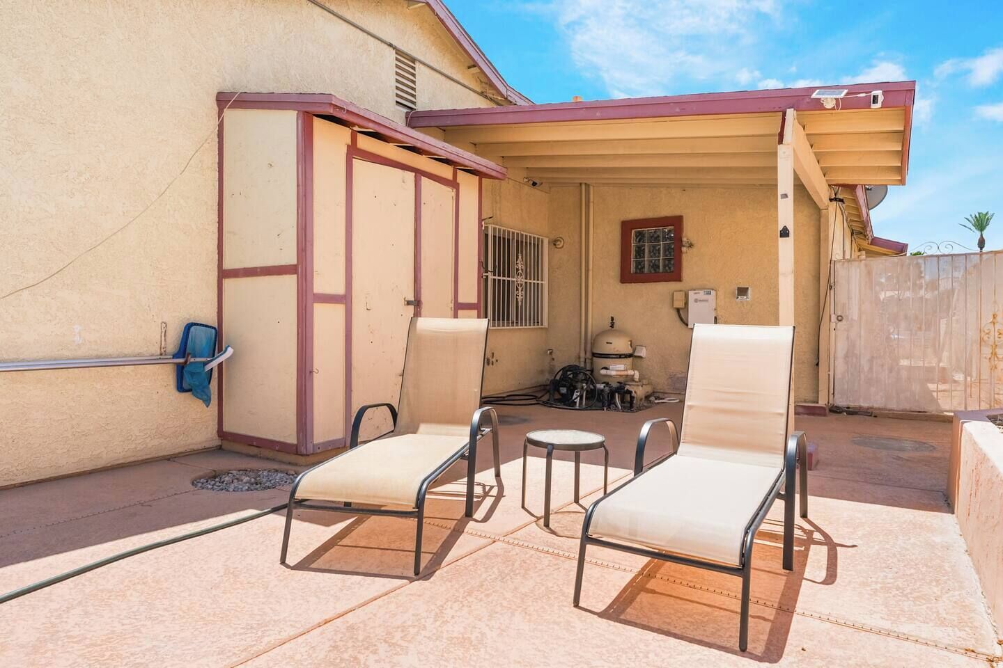 Un patio con dos sillones de descanso y una mesita, un área techada con ventana, y un calentador de agua al fondo.