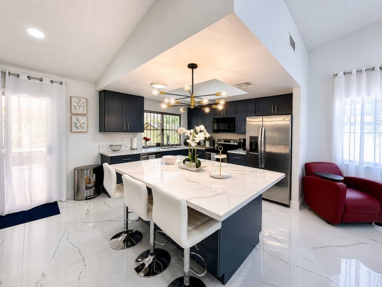 Une cuisine moderne avec un îlot central, des appareils en acier inoxydable et une chaise rouge.