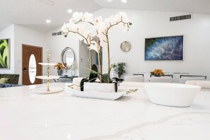 A modern living room with a marble floor, a white sofa, a coffee table, and a decorative orchid arrangement. - NEW 5BR 4.5BA Home, Pool, BBQ, 8 min to Strip (Las Vegas)