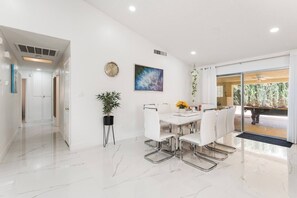 A modern dining area with a white table and chairs, a potted plant, and a painting on the wall. - NEW 5BR 4.5BA Home, Pool, BBQ, 8 min to Strip (Las Vegas)