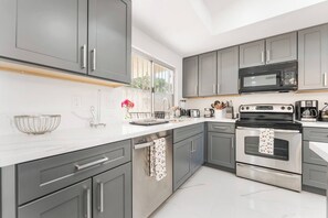 A modern kitchen with grey cabinets, stainless steel appliances, and a white countertop. - NEW 5BR 4.5BA Home, Pool, BBQ, 8 min to Strip (Las Vegas)