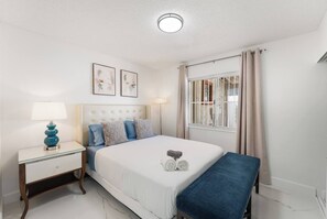 A bedroom with a bed, bedside table, lamp, and a window with curtains. - NEW 5BR 4.5BA Home, Pool, BBQ, 8 min to Strip (Las Vegas)