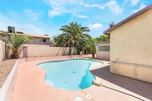 Une piscine à bord incurvé, entourée d’une terrasse en béton et de palmiers.
