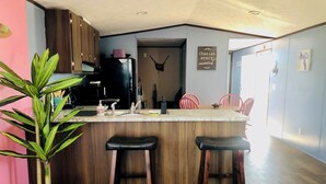 Une cuisine moderne avec des meubles en bois, un réfrigérateur noir, un tabouret de bar et une plante en pot.