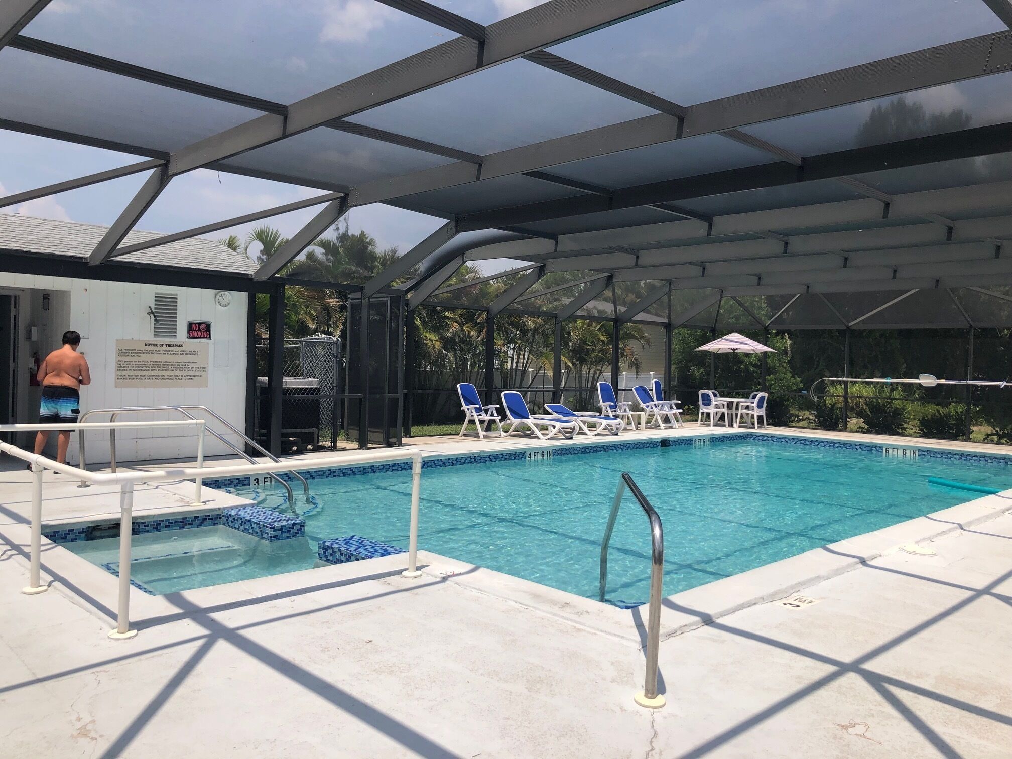 Une piscine aux carreaux bleus, un espace couvert avec des chaises longues et un panneau d’information.