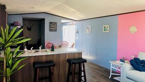 Un espace de vie compact comprenant un coin cuisine avec un comptoir-bar et des tabourets, une table à manger avec des chaises, une petite table blanche et un canapé.