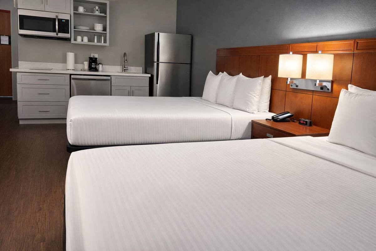 A hotel room with two beds, a wooden headboard, bedside lamps, a refrigerator, a microwave, a coffee maker, and a small desk with a phone.