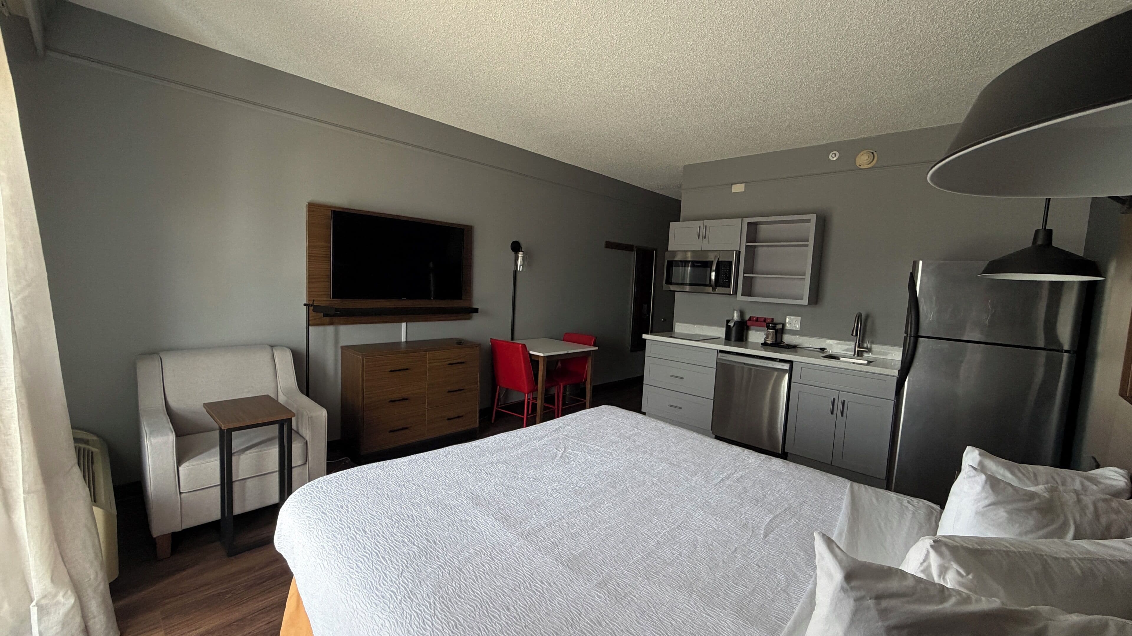 Une chambre d’hôtel équipée d’un lit, d’un bureau, d’une chaise, d’une kitchenette et d’un téléviseur.