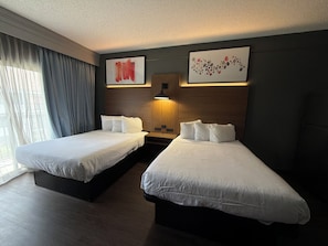 A hotel room with two beds, a wooden headboard, a large window with curtains, and artwork on the walls. - Hawthorn By Wyndham Dallas Love Field Airport (Dallas)