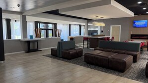 Eine moderne Hotelhalle mit Sitzgelegenheiten, einem Empfangsbereich und einem großen Fernseher.