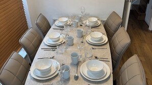 A dining table set with white plates, bowls, and glasses, surrounded by beige chairs.