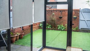 A room with a glass door leading to a garden, a wicker table, and potted plants.