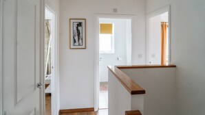 A hallway with white walls, a wooden handrail, and a framed artwork on the wall.