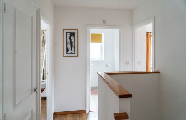 A hallway with white walls, a wooden handrail, and a framed artwork on the wall.