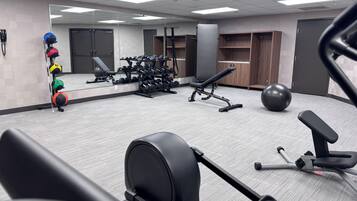 A gym with exercise equipment, a bench, a mirror, and lockers.