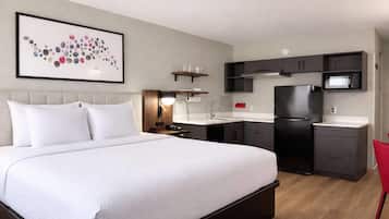 A modern hotel room with a large bed, a kitchenette, a microwave, and a red chair.