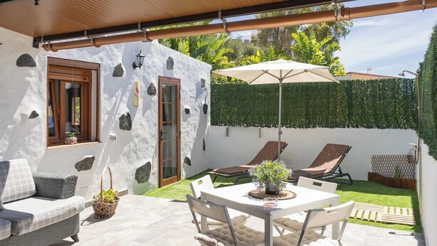 Un patio cubierto con una mesa y sillas, un rincón de descanso con un sofá y una planta decorativa.