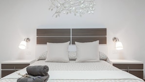 Un dormitorio moderno con una cama grande, dos mesitas de noche, un adorno en la pared y dos lámparas de pared.