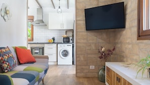 Cocina moderna con armarios blancos, microondas y lavadora. Hay un televisor de pantalla plana montado en la pared.