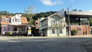 A street with buildings, including a pizza restaurant and a building with a sign that says "Hotel Marie Confitairia". - Casarão da Vila Smart Hospedaria (Blumenau)