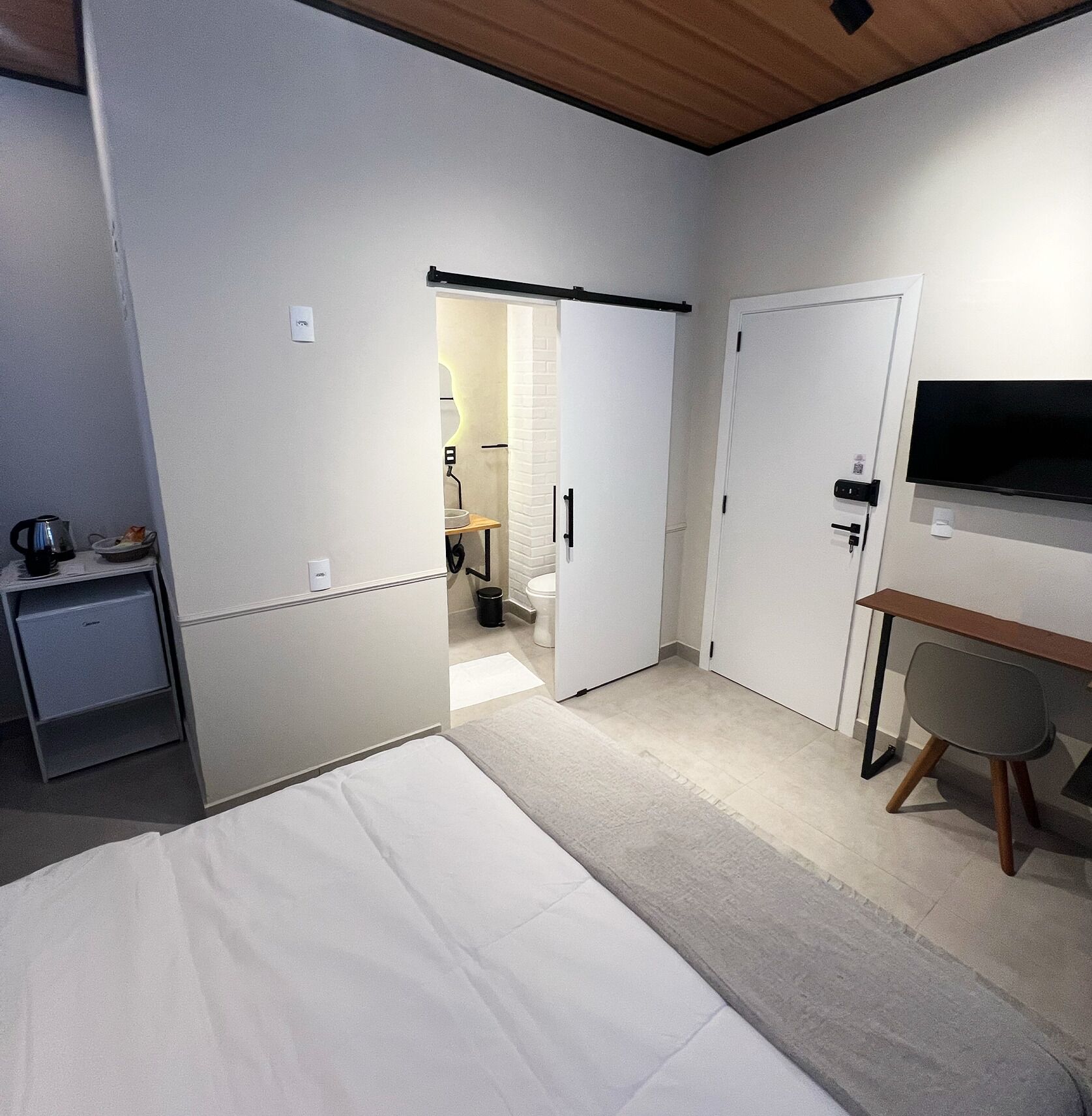Une petite chambre comprenant un lit, un bureau, une télévision et une porte donnant sur une salle de bain.