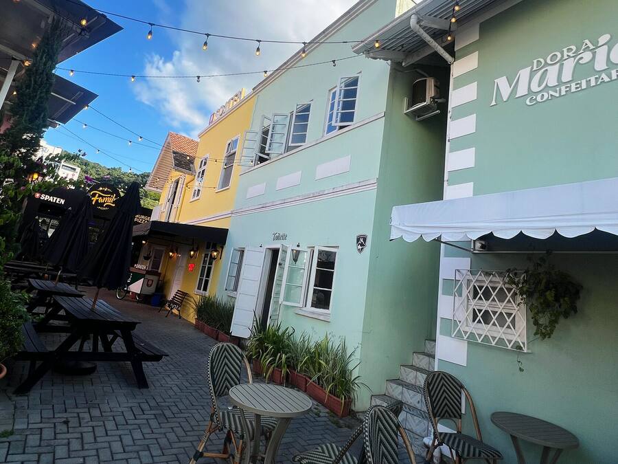 Un espacio al aire libre con encanto, con mesas de madera y sillas de mimbre, rodeado de edificios coloridos con letreros de un restaurante y una tienda de confeti.