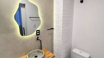 A bathroom with a white toilet, a round sink with a mirror, and a wooden countertop.