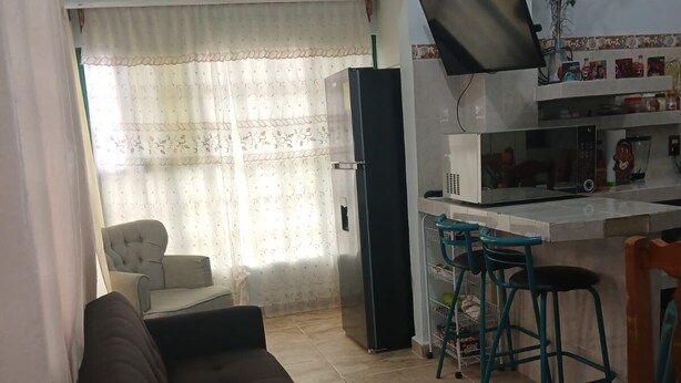 A living room with a sofa, a dining area with a table and chairs, a kitchen with a microwave, and a refrigerator.