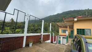A building with a fenced patio area, a parked car, and a mountainous backdrop.