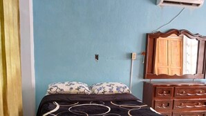 A bedroom with a bed, a dresser, an air conditioning unit, and a mirror.