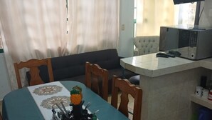 A dining area with a table set for four, a microwave, and a small kitchen area.