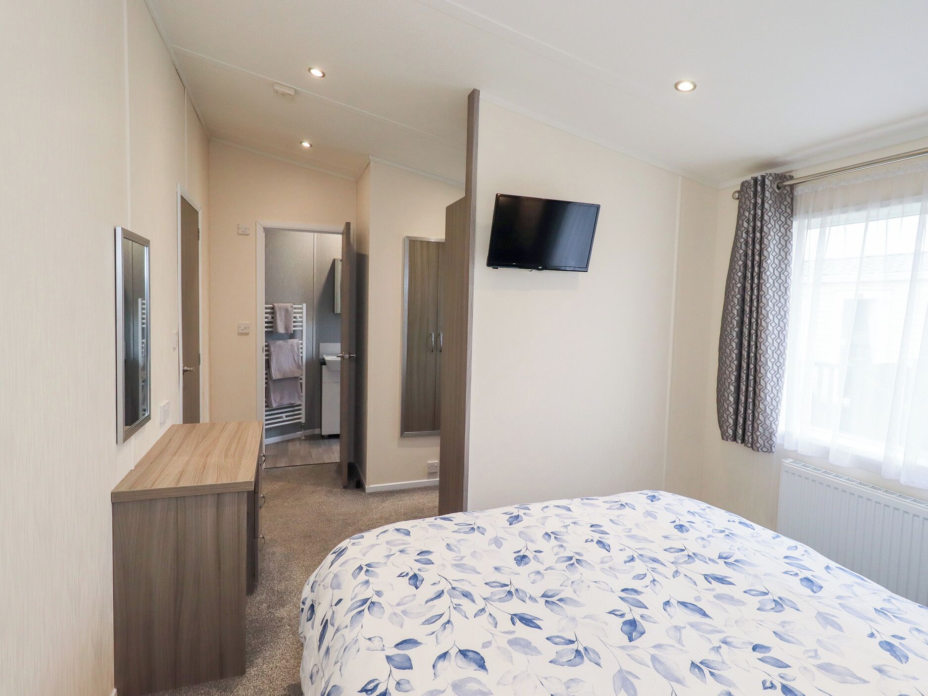 Una habitación de hotel con cama, televisor montado en la pared, armario y vestidor.