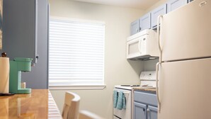 A compact kitchen with a wooden table, a coffee machine, a stove, and a refrigerator. - Anchor Point at Oak Shores! 5-min walk to beach (Biloxi)
