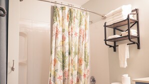 A bathroom with a shower curtain featuring a floral pattern, a bathtub, a toilet, and a towel rack with folded towels. - Anchor Point at Oak Shores! 5-min walk to beach (Biloxi)